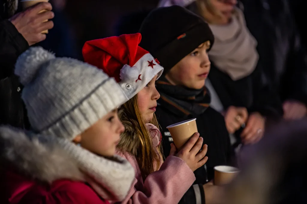 Trois enfants habillés chaudement fixent un point à droite et sont captivés.